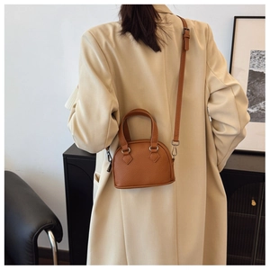 Detail of caramel lychee grain leather mini shell bag worn as a crossbody with a slim strap