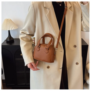 Close-up of brown pebbled leather mini dome bag worn by model in minimalist home setting