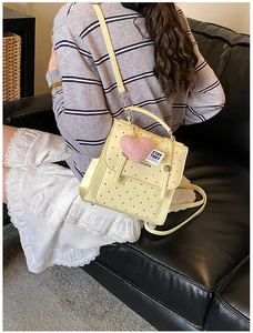 Close-up of beige polka dot backpack with plush heart charm and premium leather texture
