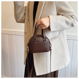 Detail of a dark brown shell-shaped crossbody bag worn with an elegant wool blazer