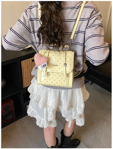 Detail view of yellow polka dot backpack with a pink heart plush charm on a child model