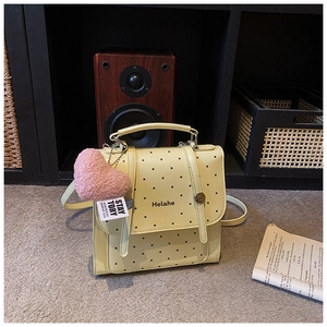 Detail of a light yellow polka dot kid's backpack with a pink heart plush charm