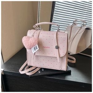 Pink polka dot PU leather backpack with a plush heart charm for girls shown on desk