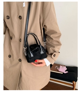 Primer plano de un mini bolso bandolera negro con lazo llevado por una modelo en un set
