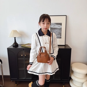 Brown shell-shaped leather kids handbag with adjustable strap shown in home setting