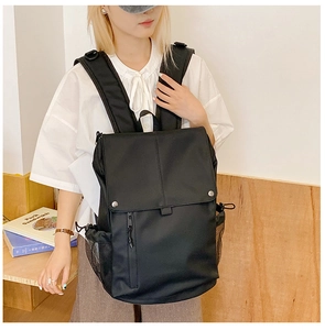 Detail view of black school backpack with mesh side pocket and flap closure on model