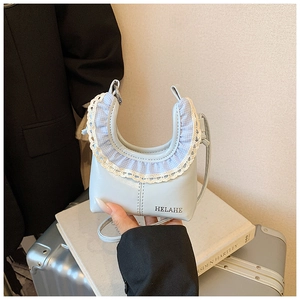 Detail of light blue crescent bag with white lace trim and metal logo by a suitcase