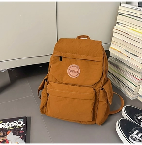 Détail du sac à dos en nylon caramel avec écusson KEMI en cuir dans un décor scolaire