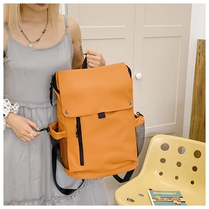 Detail view of the ginger yellow multi-pocket backpack held by a model in a room