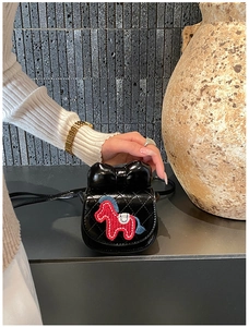 Détail d'un mini sac matelassé noir avec nœud et écusson poney rouge sur fond texturé