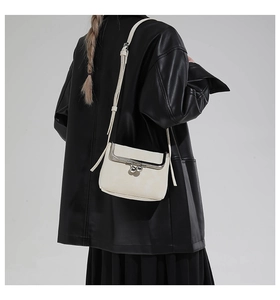 Detail view of a cream mini crossbody doctor bag with silver ball clasp on a black jacket