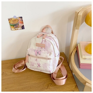Detail of canvas mini backpack featuring butterfly prints and branding on wooden table