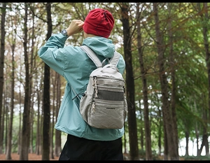 Zaino outdoor in nylon grigio chiaro con cerniere multiple mostrato nel bosco