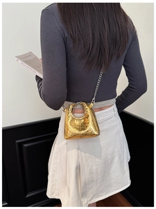 Detail of a mini gold crossbody bag with heart quilted pattern on a fashion model back