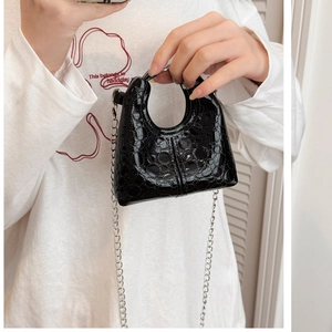 Close-up of mini black patent leather handbag with silver chain and glossy finish