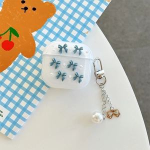 Detail of matte Airpods case with blue bows, pearls and a metal butterfly keychain