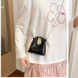 Close-up of mini black faux leather bag with silver chain strap worn by a child
