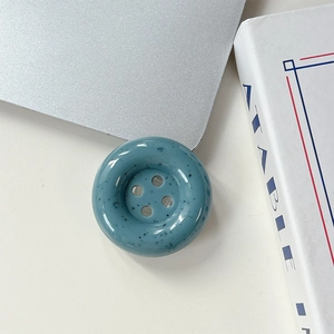Gros plan d'un support de téléphone bouton sarcelle à taches noires sur table blanche