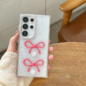 Detailed view of pink 3D bows and pearl charms on a glittery phone case for Samsung S24