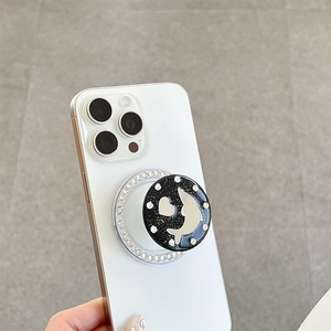 Detail of a black rhinestones phone griptok with silver dolphin and heart on a white phone