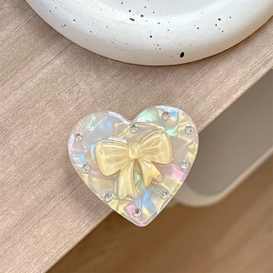 Detailed view of iridescent heart phone grip with yellow bow and sparkling rhinestones