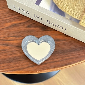 Macro shot of heart-shaped glitter phone mirror on vintage book with warm knit sweater