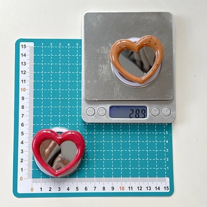 Macro detail of heart-shaped phone mirror showing dimensions of 5.5cm and 28.9g weight