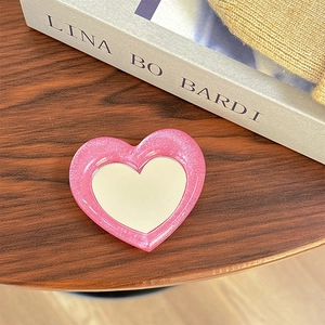 Close-up of heart-shaped pink glitter makeup mirror phone grip on a wooden desk