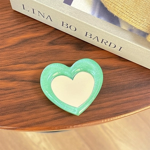 Detail of a green glitter heart-shaped phone mirror socket on a dark wooden table