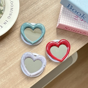 Macro view of heart-shaped MagSafe mirror phone grips in three colors on a wooden table