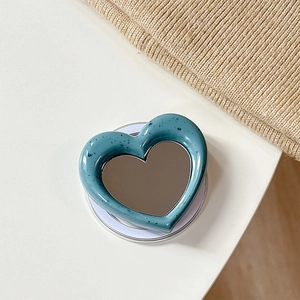 Detail of blue heart-shaped MagSafe phone mirror grip on a soft knitted background