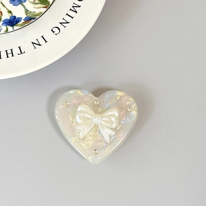 Support de téléphone cœur irisé avec nœud blanc et strass sur un plateau céramique