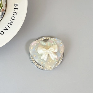 Détail du support téléphone cœur avec texture irisée, nœud blanc et strass