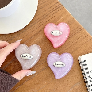 Close-up of heart-shaped glitter phone grips with handmade metal plates on a desk