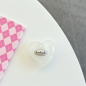 Detail of pearlescent white heart phone grip with handmade text on a white surface