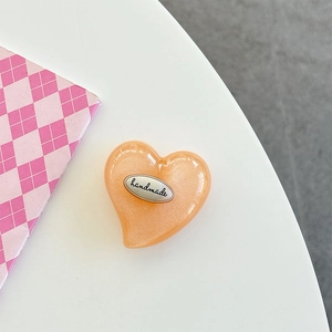 Close-up of heart-shaped phone grip with orange glitter resin and handmade metal plate