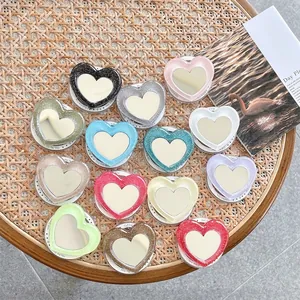 Glitter heart-shaped foldable phone socket mirrors in multiple colors on a textured mat