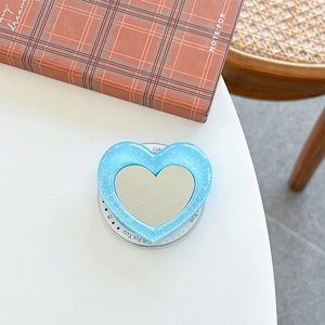 Glittery blue heart-shaped phone griptok with a built-in makeup mirror on a white table