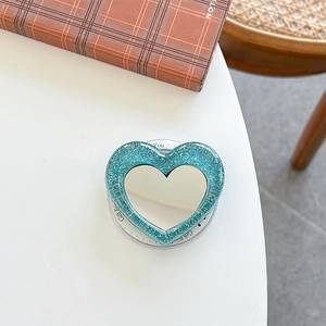 Detail of blue glitter heart phone socket mirror with retractable grip on white desk
