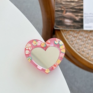 Detail of pink heart phone grip with fruit motifs and built-in vanity mirror on a table