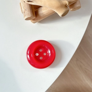 Close-up of a bright red four-hole resin button phone grip on a clean white desk