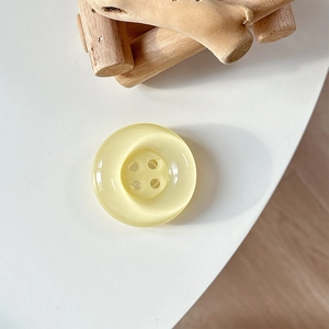 Detail of a round resin button phone grip featuring a creamy yellow cat-eye stone texture