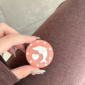 Macro view of a round glittery phone grip featuring a white dolphin and heart motif