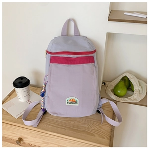 Detail of light purple canvas backpack with red zipper and woven charm on wooden furniture