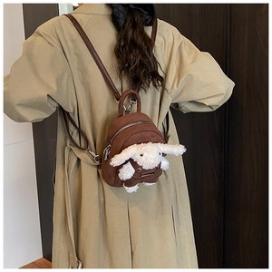Detail view of a cute plush bunny doll on a brown suede toddler backpack with slim straps