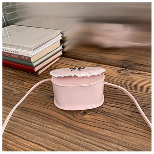 Detail of pink girls' crossbody bag featuring white lace trim and bow graphic on a wooden desk
