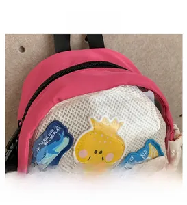 Dettaglio dello zaino rosa per bambini con tasca a rete bianca e toppe ricamate con cartoni