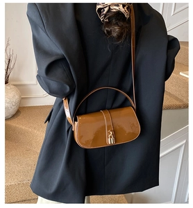 Brown patent leather shoulder bag with gold clasp shown on model in a minimalist setting