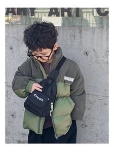 Detail of trendy children's black chest bag with Dream text on olive green colorblock jacket