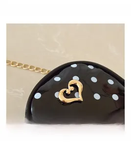 Detail der schwarzen gepunkteten Lackledertasche mit goldenem Herz-Verschluss und Kette